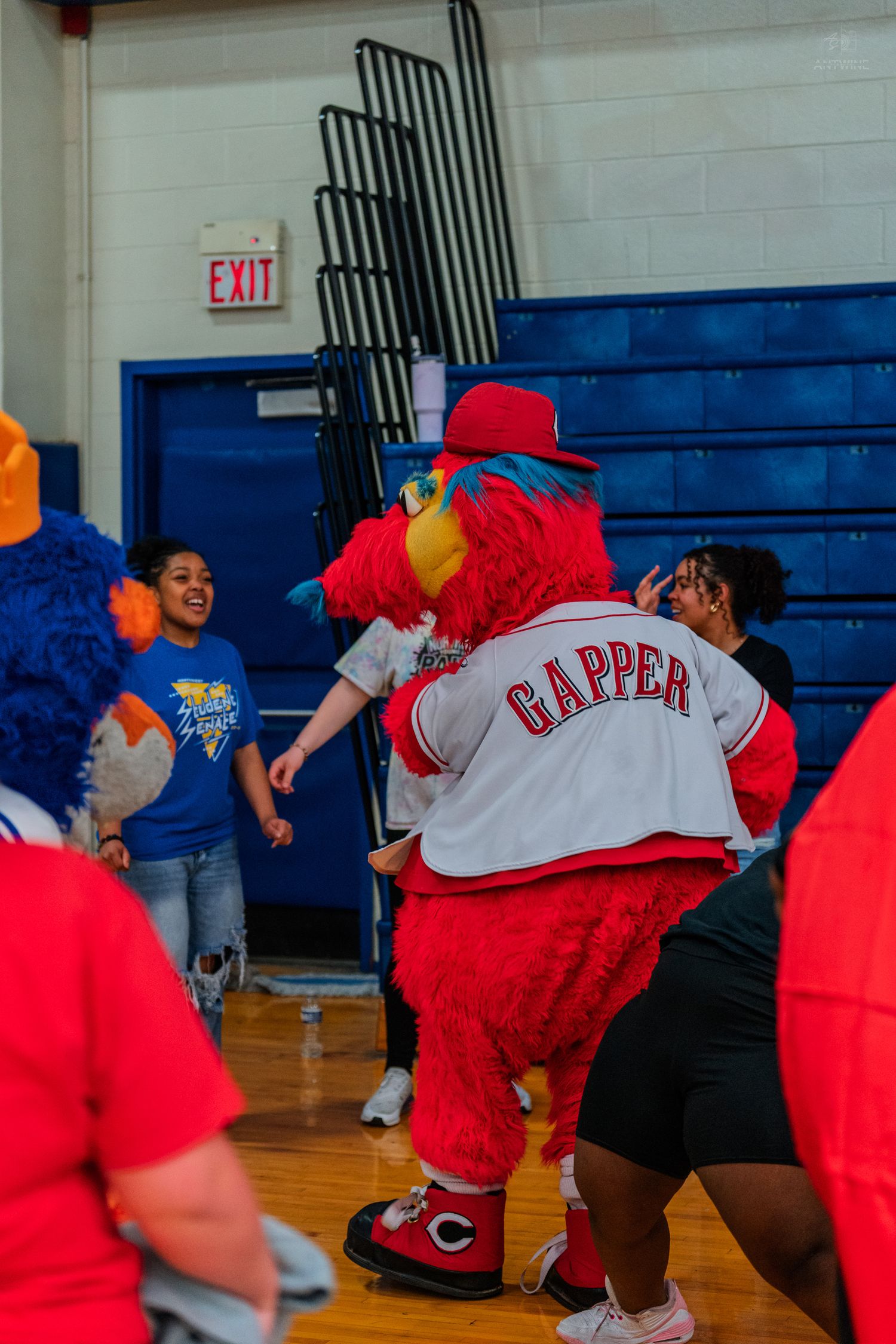 Gapper, the Cincinnati Reds red bird mascot, dances with children in a school gymnasium.