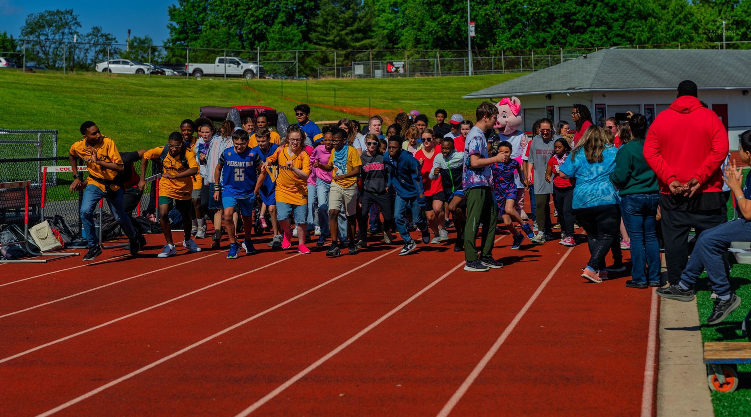 Children lined up at the starting line on a red running track during a school field day event outdoors.