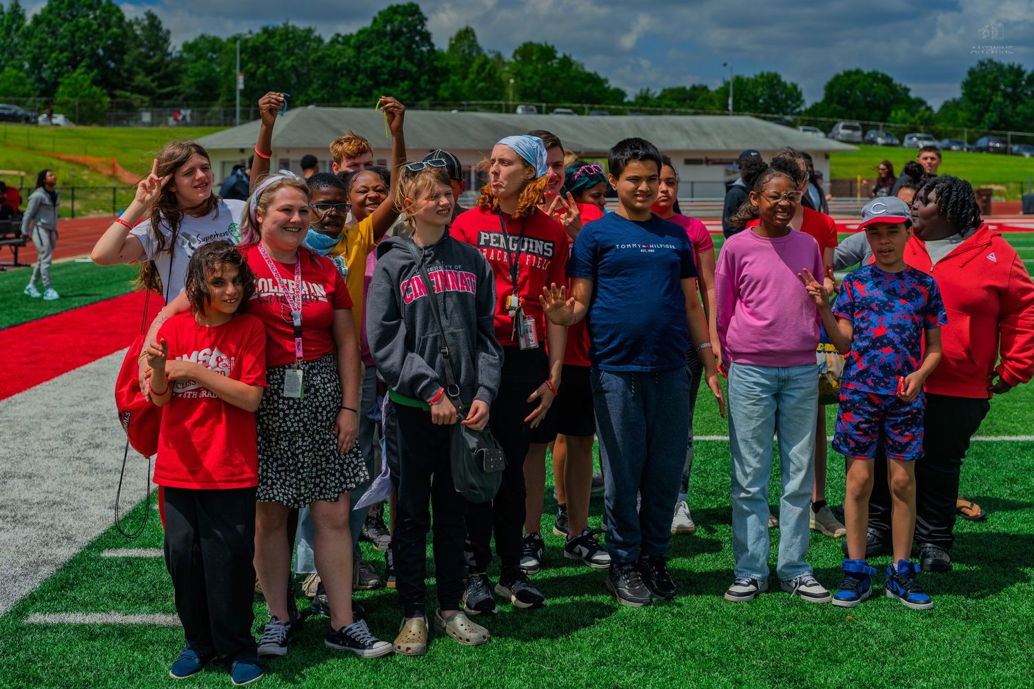 Group of students and adults posing together on a red turf football field during an outdoor school event.