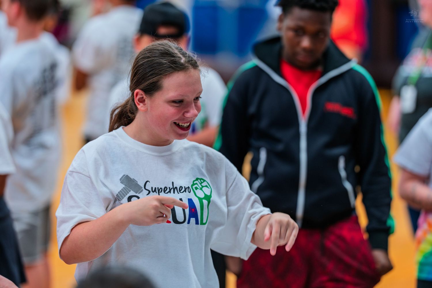 Young woman in Superhero Squad shirt laughing and dancing at an outdoor team event with diverse group.