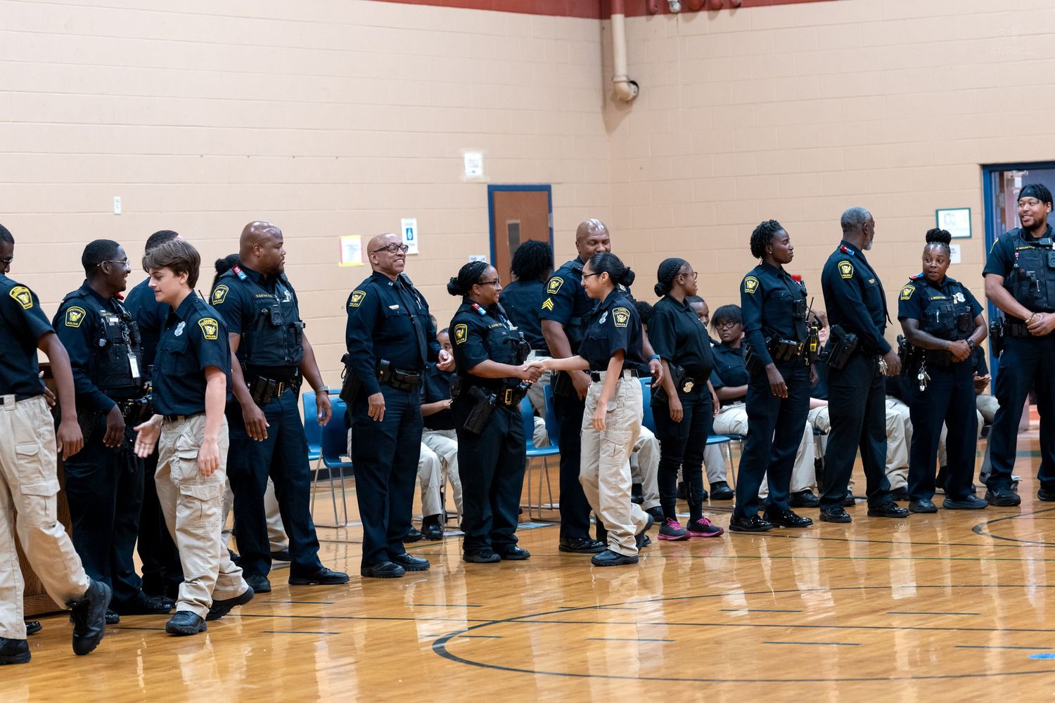 Police officers in uniform standing in a line during an indoor ceremony in a gymnasium.