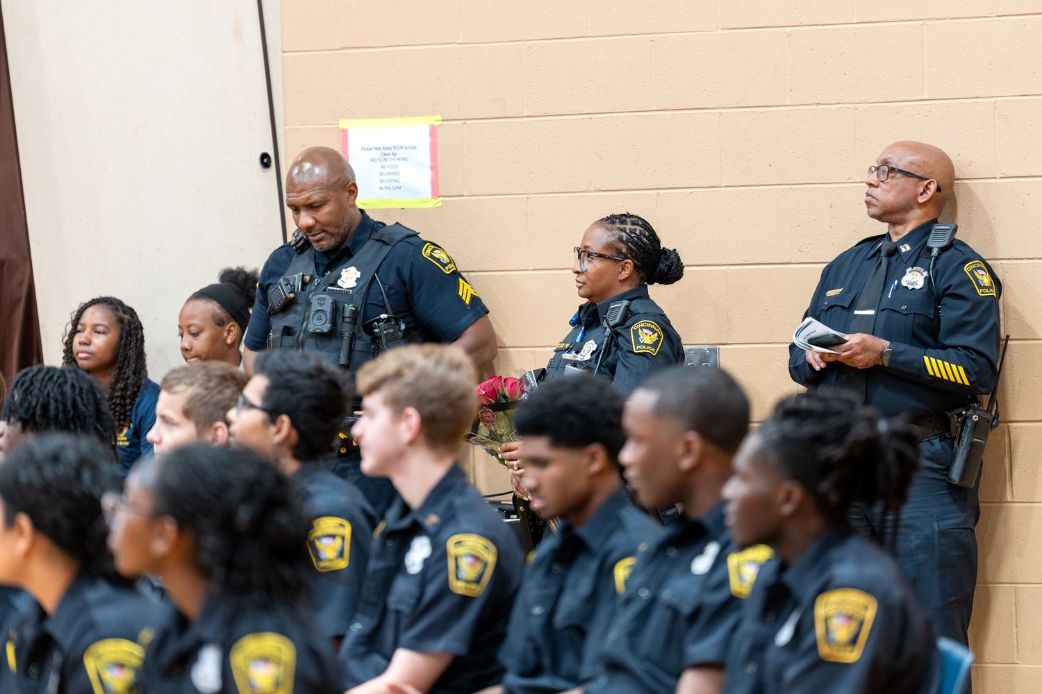 Police officers and cadets in uniform attend an indoor law enforcement training or graduation ceremony.