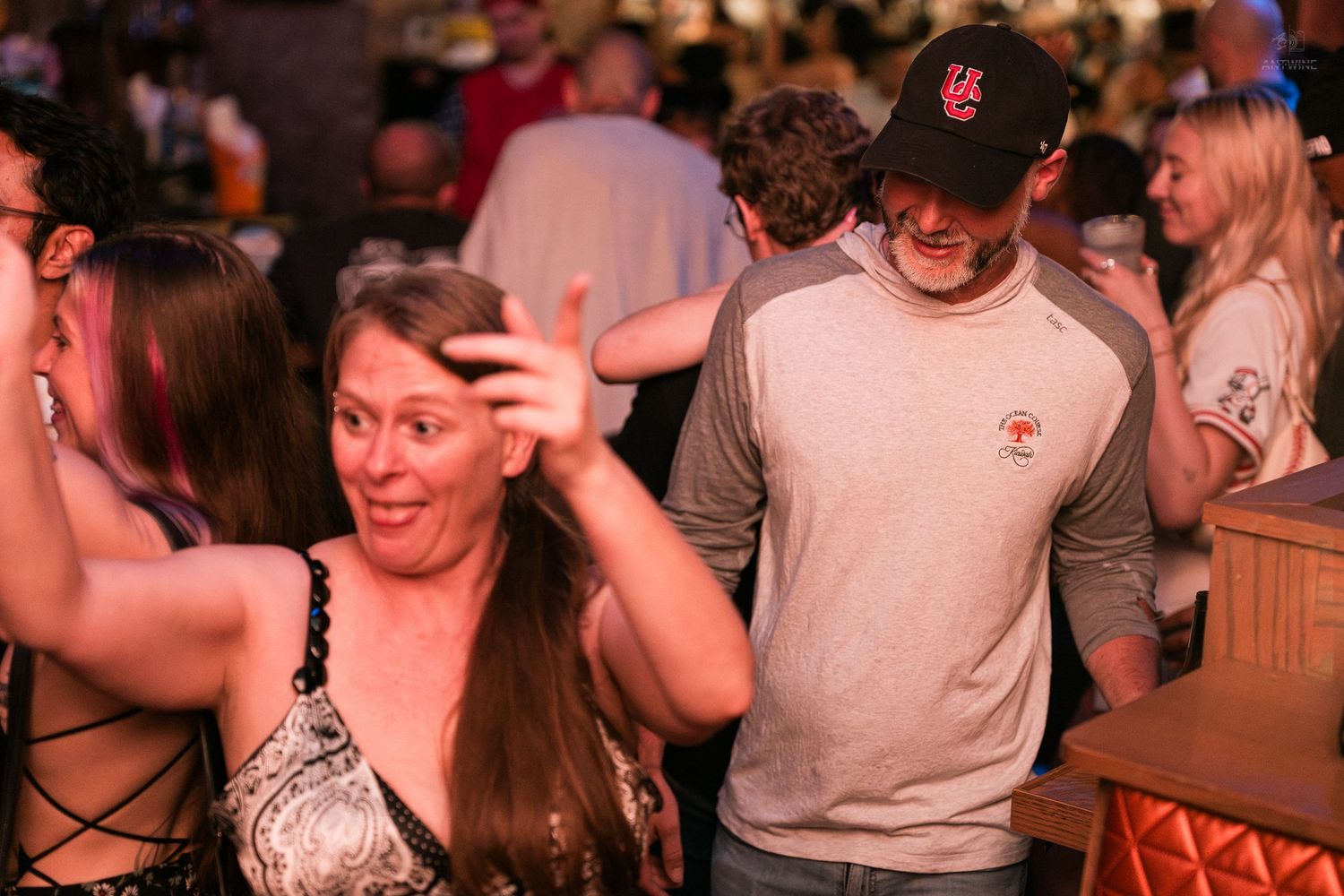 Two people socializing and taking selfie in crowded dimly lit bar at night.