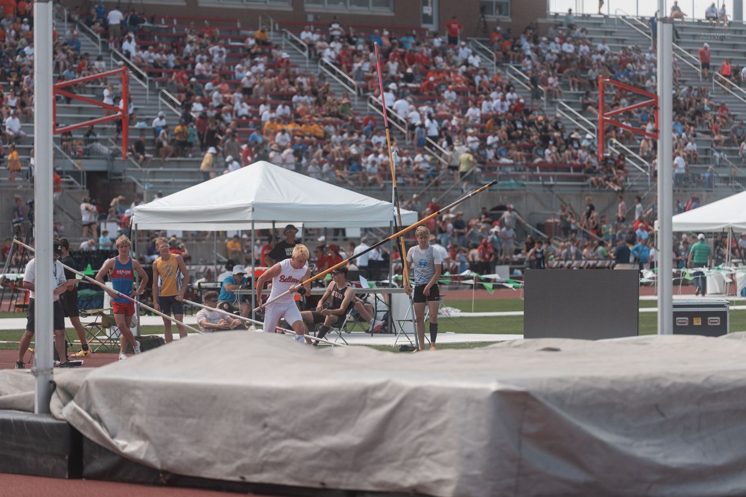 Athletes compete in pole vault at a packed outdoor track and field stadium competition.