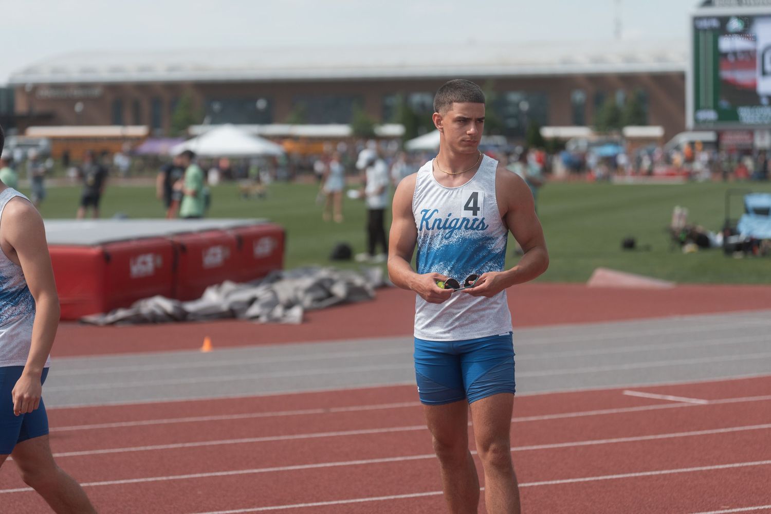 Male track athlete wearing Knights number 4 jersey walks on red track during outdoor athletics meet.