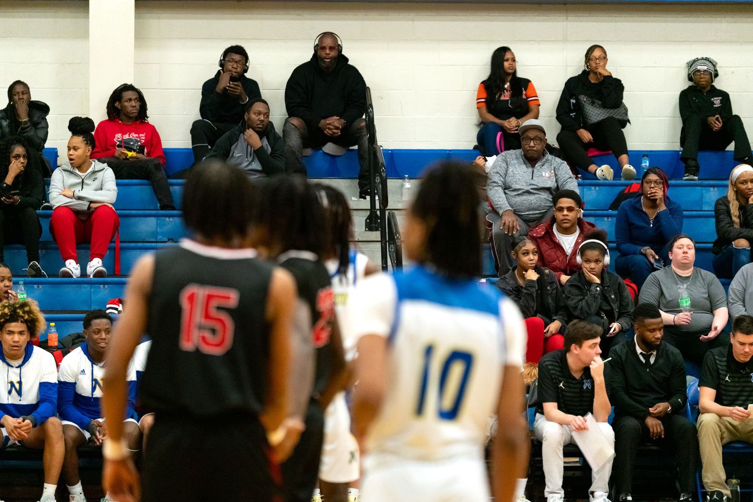 Spectators fill the bleachers watching a high school basketball game between teams in black and white uniforms.
