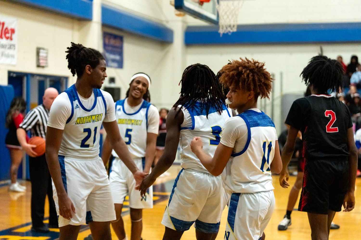 High school basketball players in blue and white uniforms huddle together on the court during a game.
