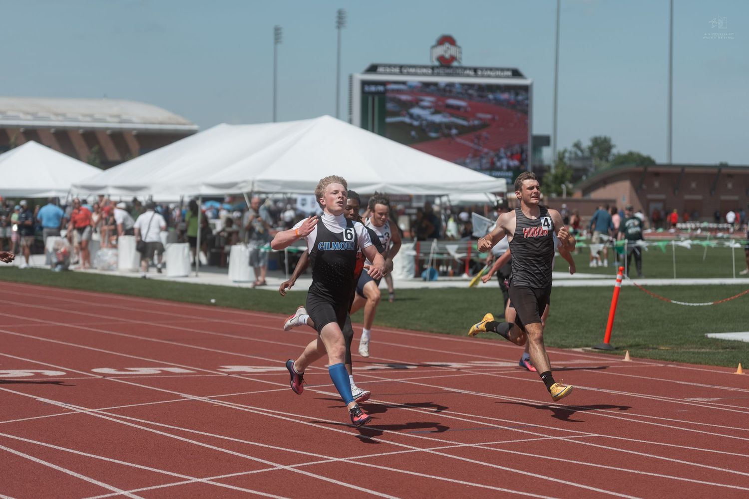 Two male sprinters race toward the finish line at an outdoor track and field competition.