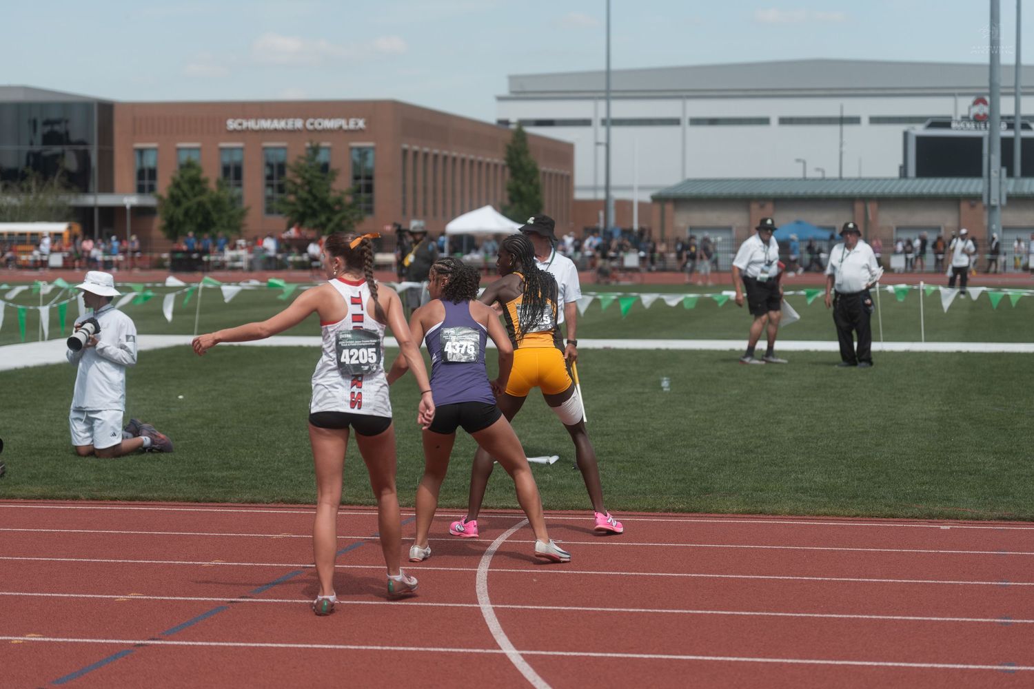 Track and field athletes exchange a relay baton during a race at an outdoor stadium competition.