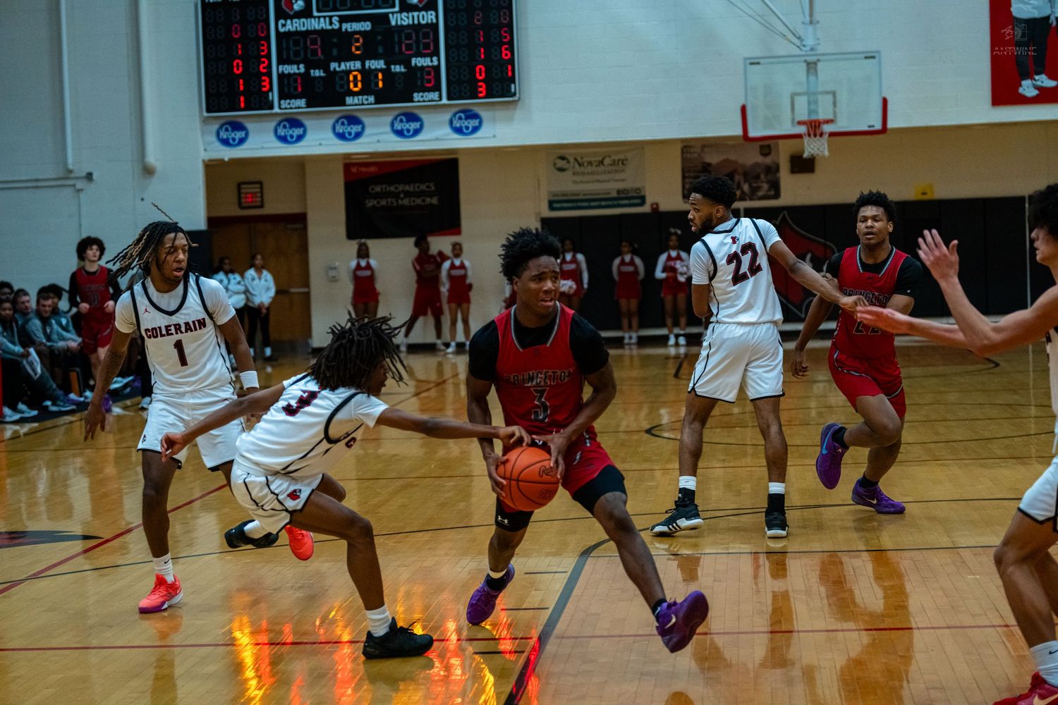 Red-uniformed player drives through Colerain defenders during packed high school basketball game.