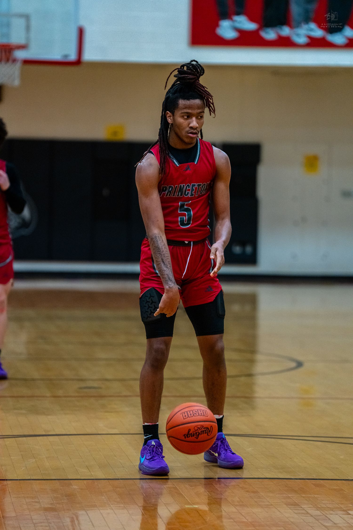Princeton #5 basketball player with dreadlocks dribbles ball during high school game in red uniform.
