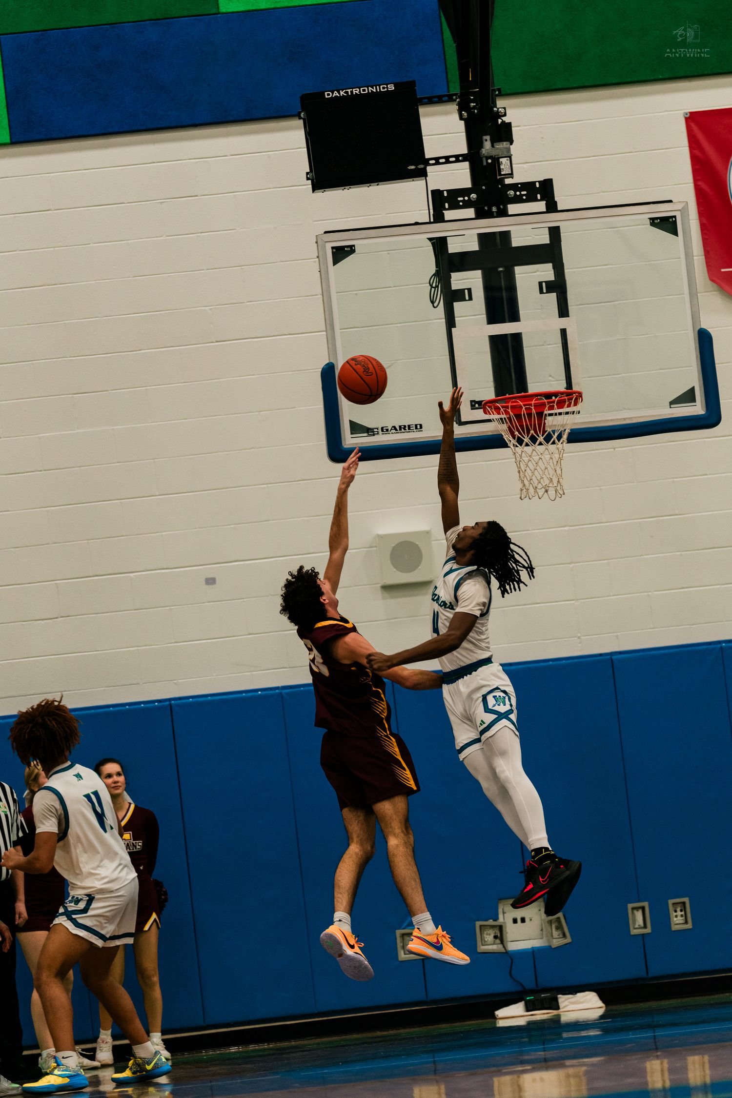 Two players leap simultaneously near the basket as one attempts a shot during a high school basketball game.