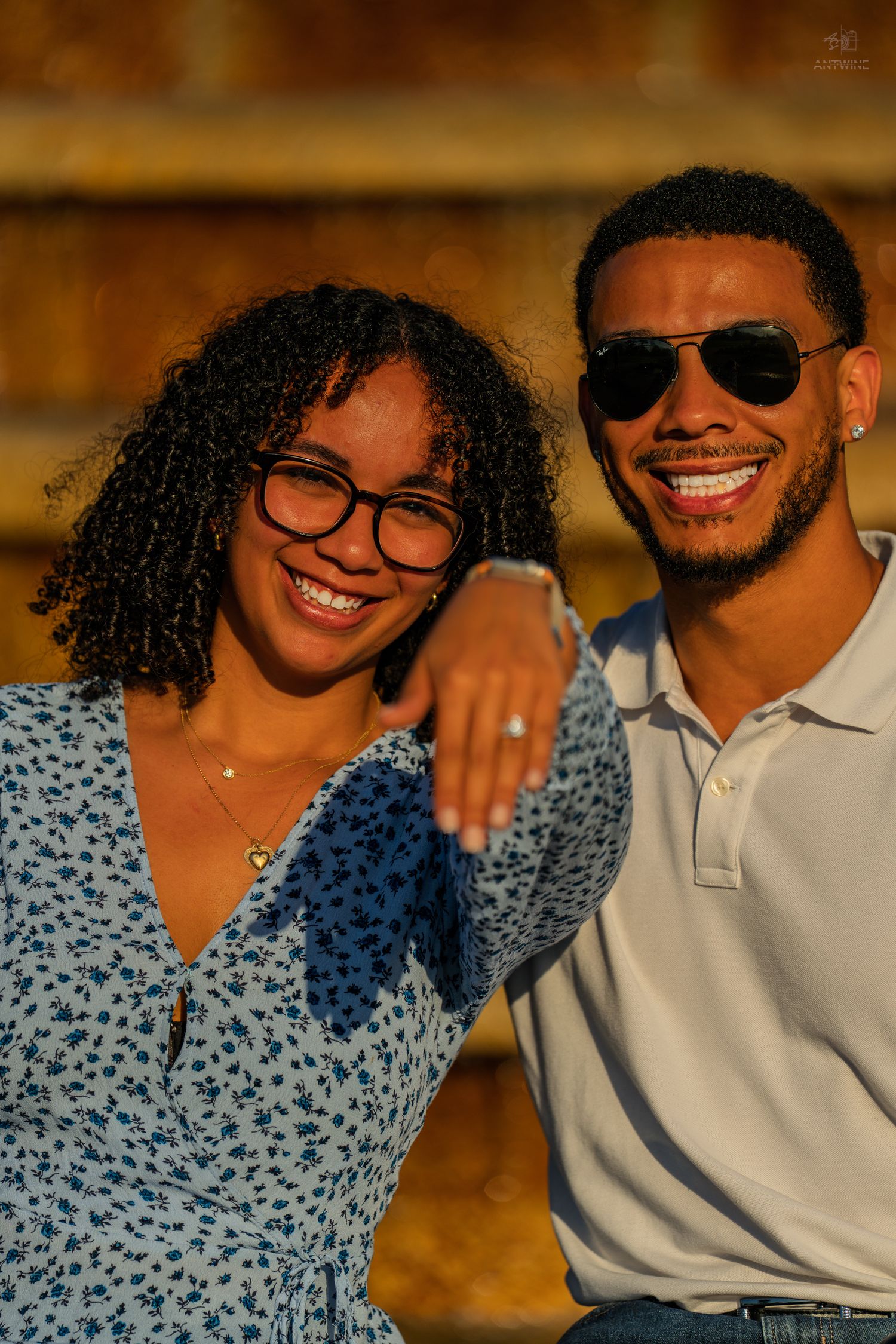 A smiling Black couple poses outdoors in warm golden light, the man with his arm around the woman.