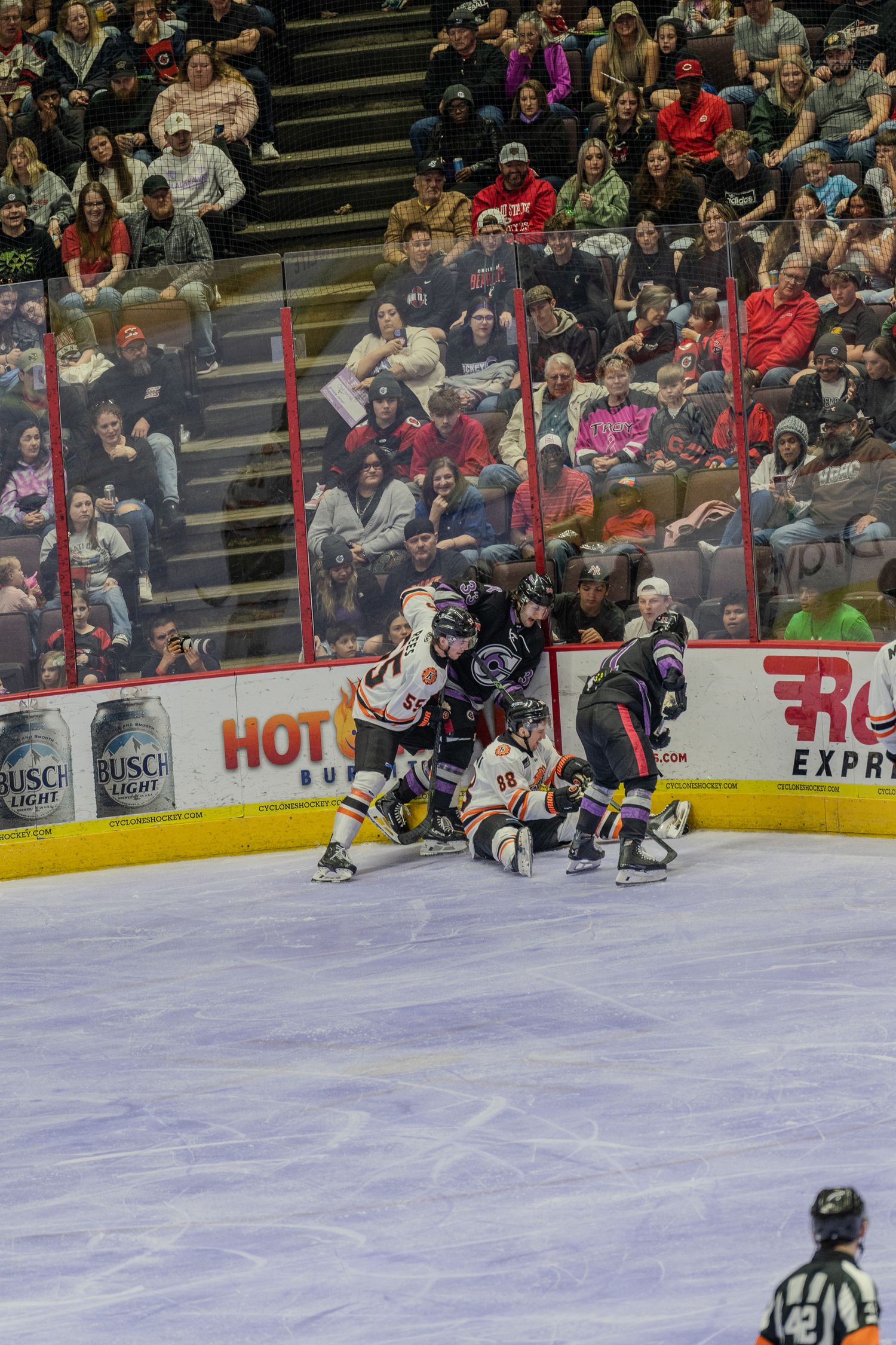 Hockey players collide along the boards during a physical minor league game with a packed crowd watching.