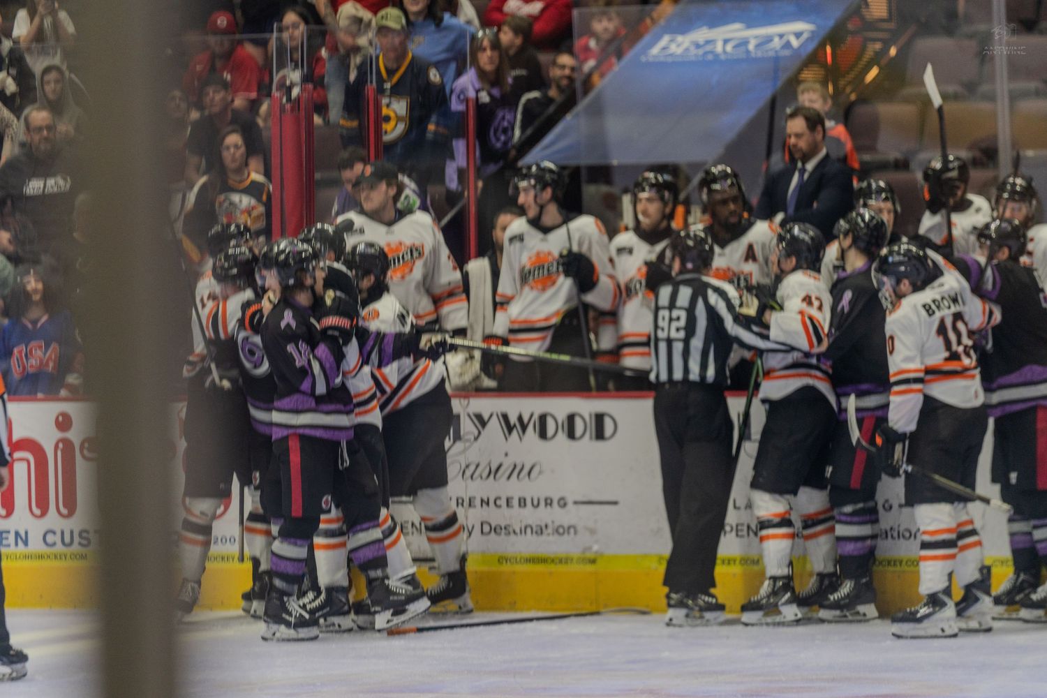 Two hockey teams converge in a scrum near the boards during an intense minor league hockey game.