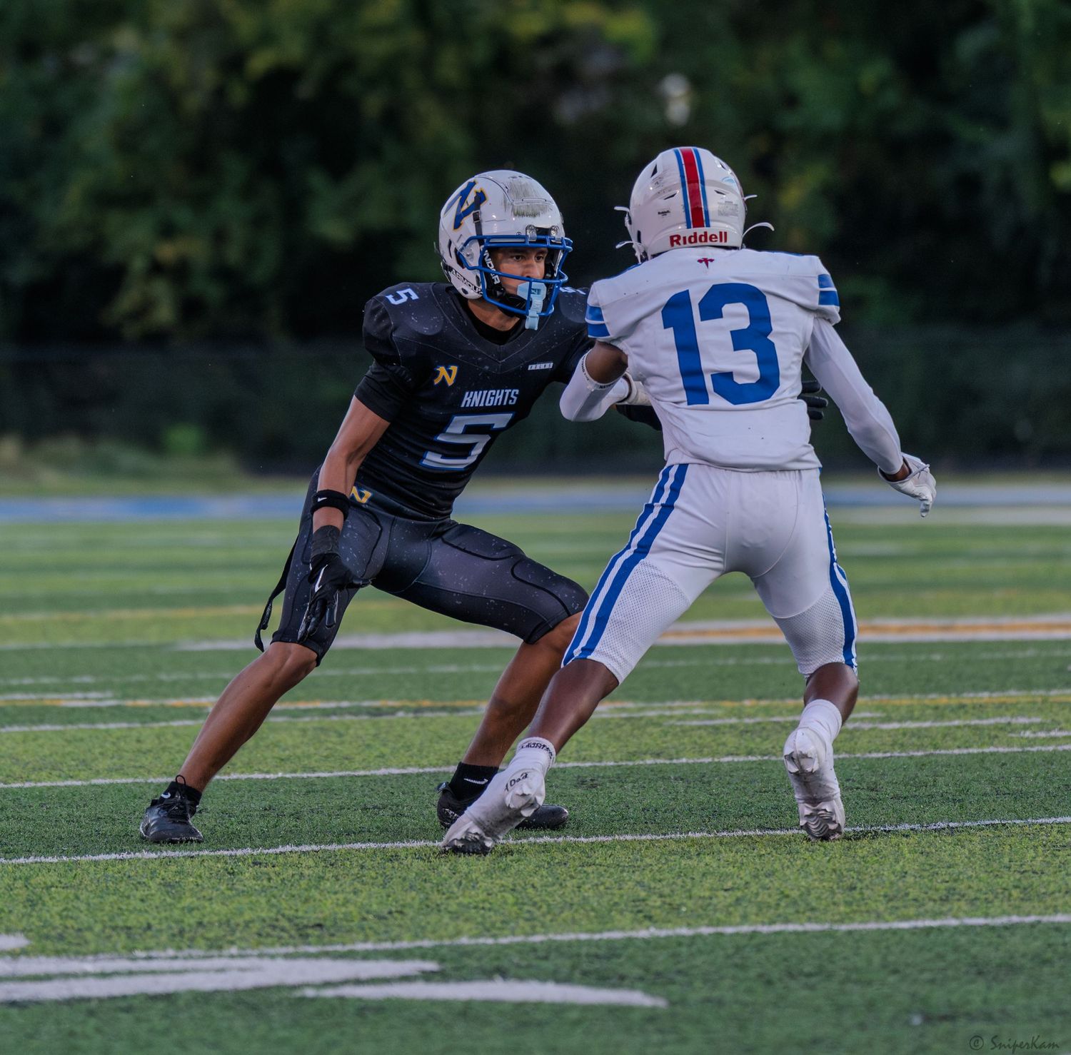 Knights defender in black uniform squares up against opponent number 13 on turf field.