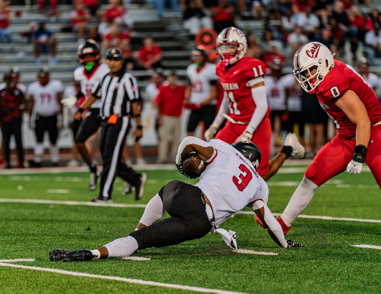 A football player slides to the ground as an opponent approaches during a high school football game.