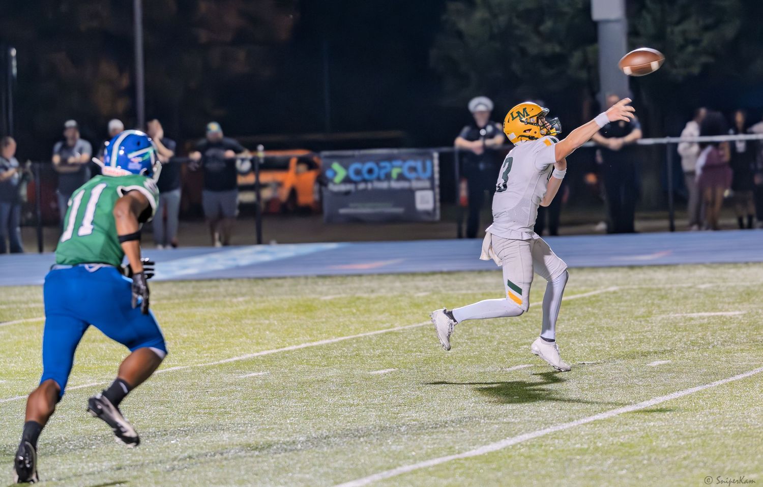 Football quarterback in white uniform throws pass while defender in green jersey applies pressure.