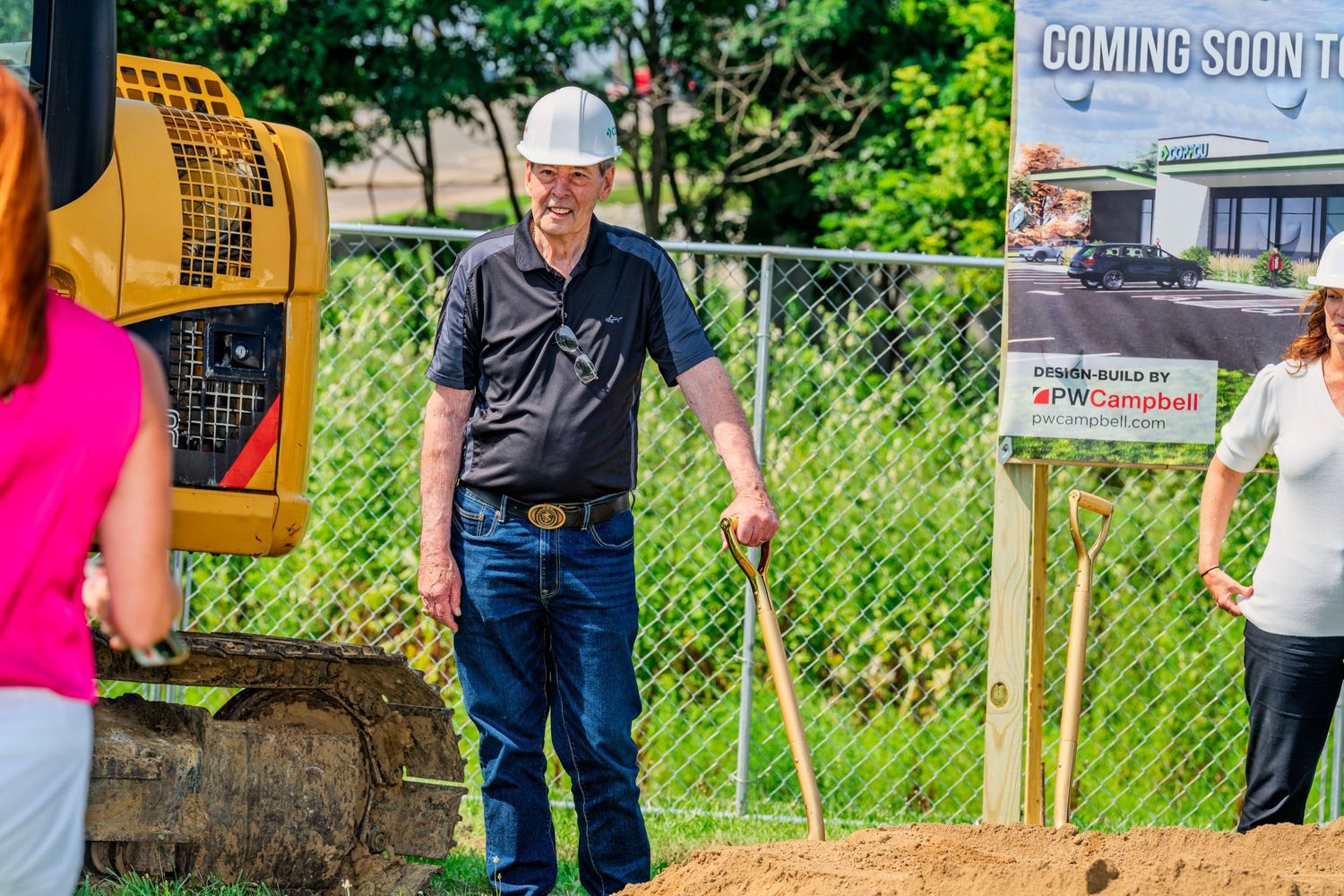 Man in hard hat smiling at outdoor groundbreaking ceremony construction site event.