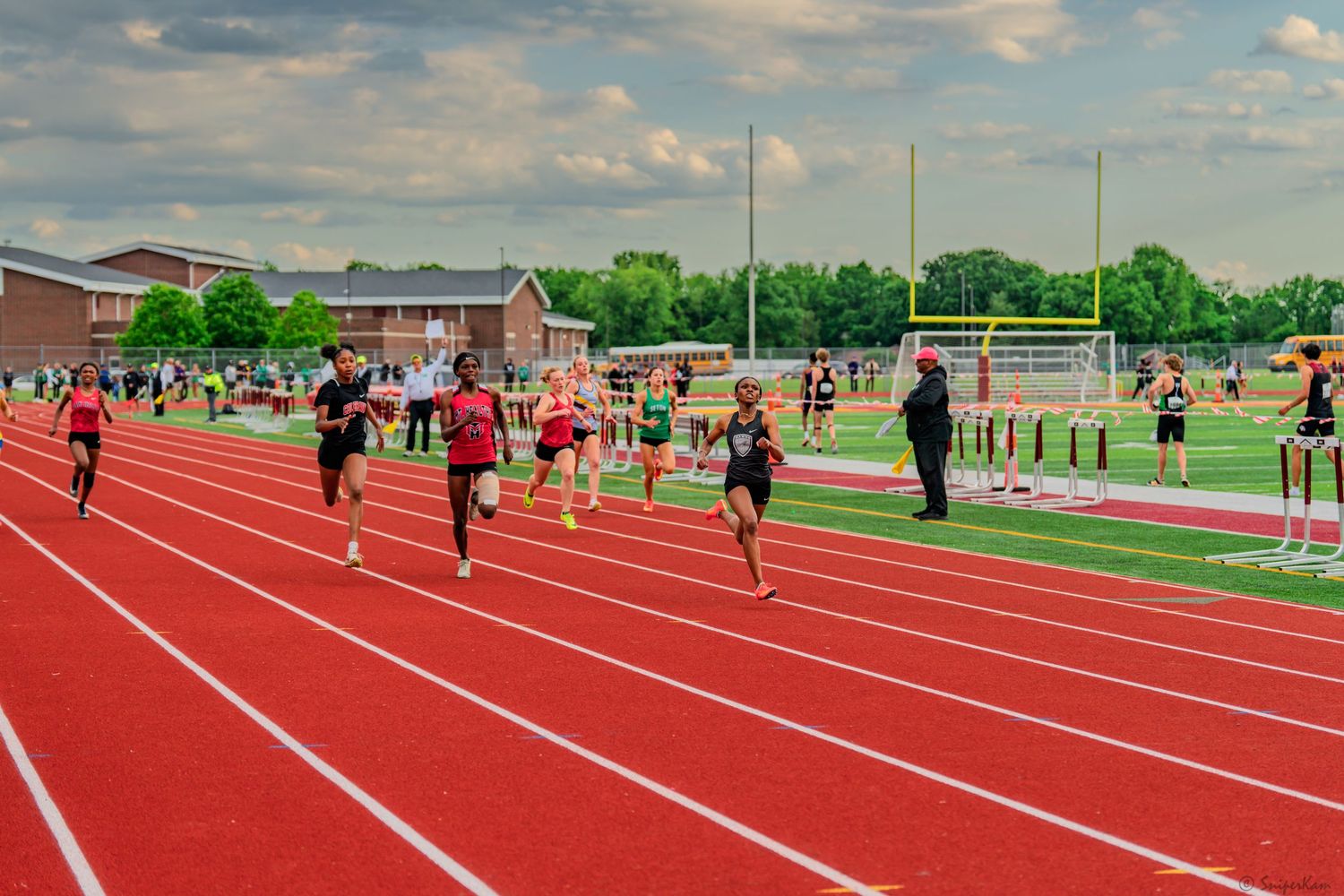 Multiple athletes sprint down red track lanes during a competitive high school track and field meet.