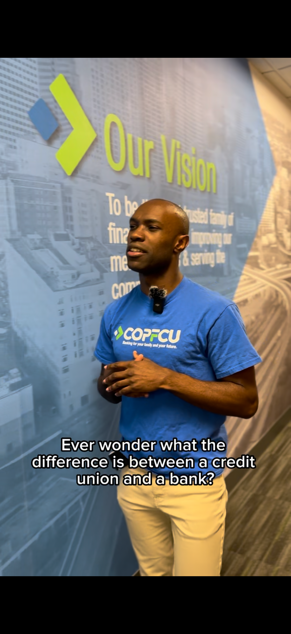 Man in COPFCU blue shirt speaks in front of Our Vision wall mural at a credit union office.