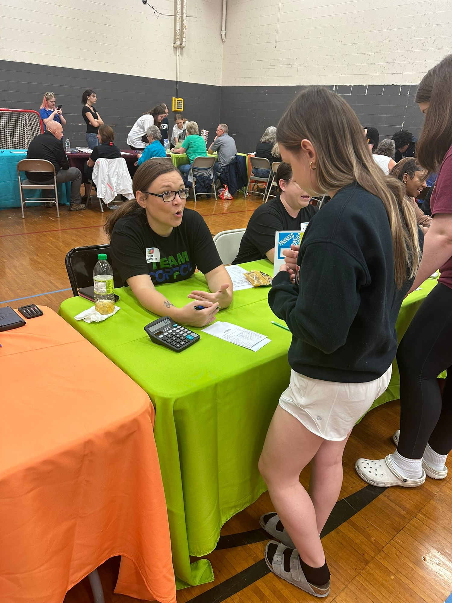 Students engage with a representative at a green table during a school career fair in a gymnasium.
