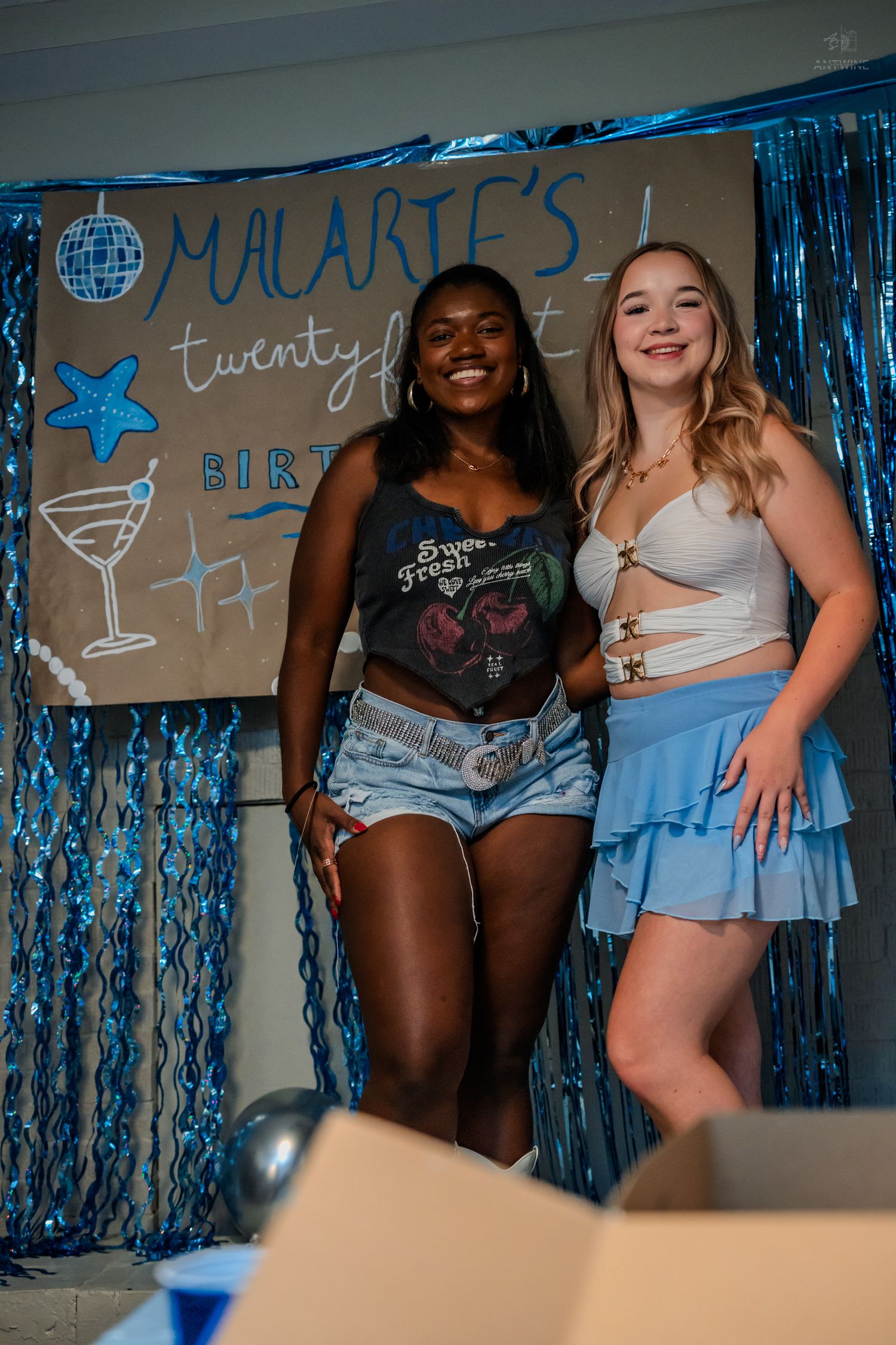 Two young women laughing together at a blue-themed 21st birthday party celebration.