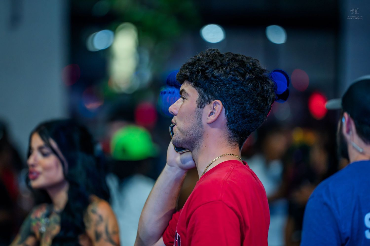 Young man in a red shirt looking up thoughtfully in a crowded nightclub.