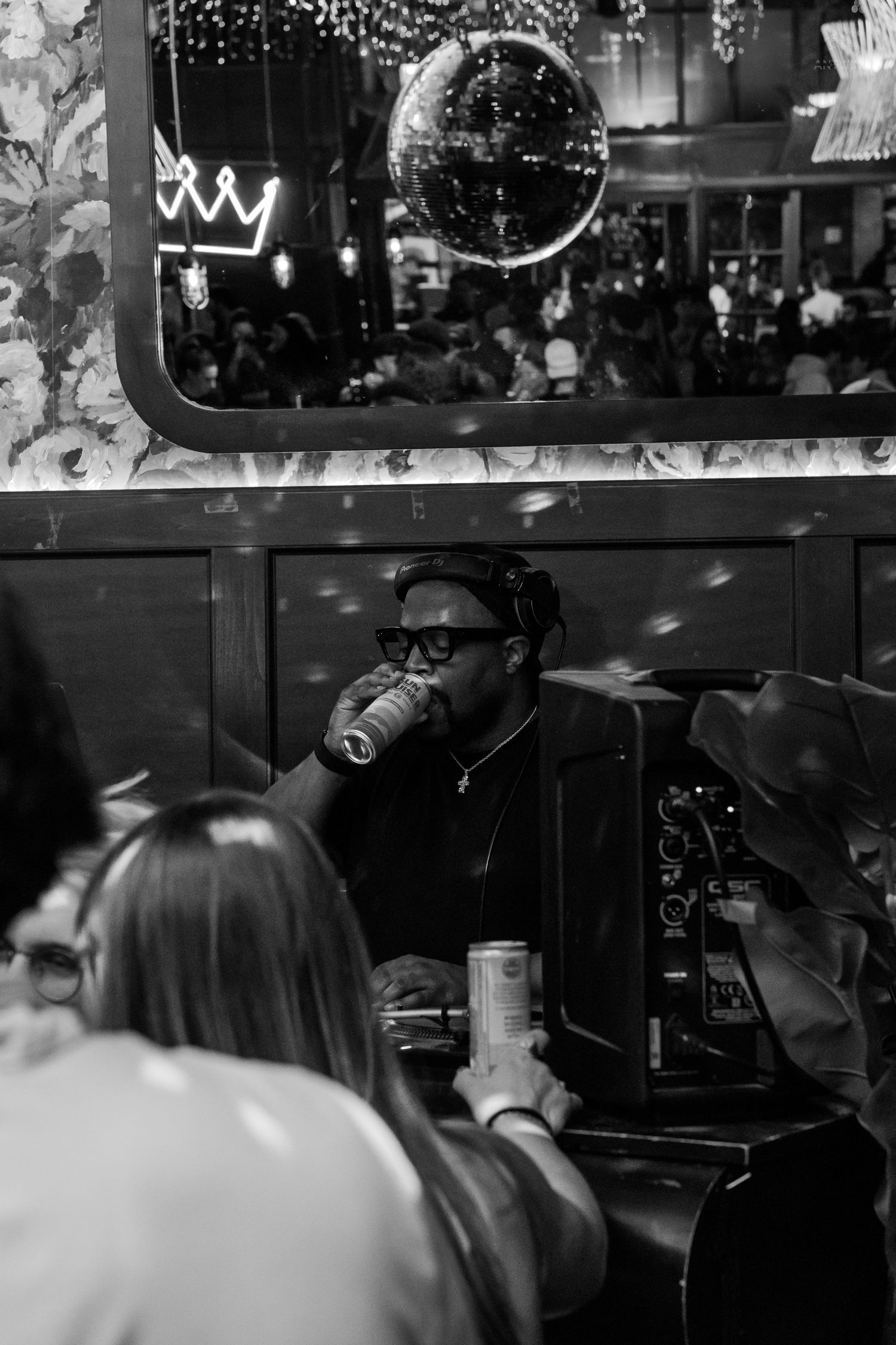 Black and white photo of a man drinking from a can at a bar booth with a mirror reflection behind him.