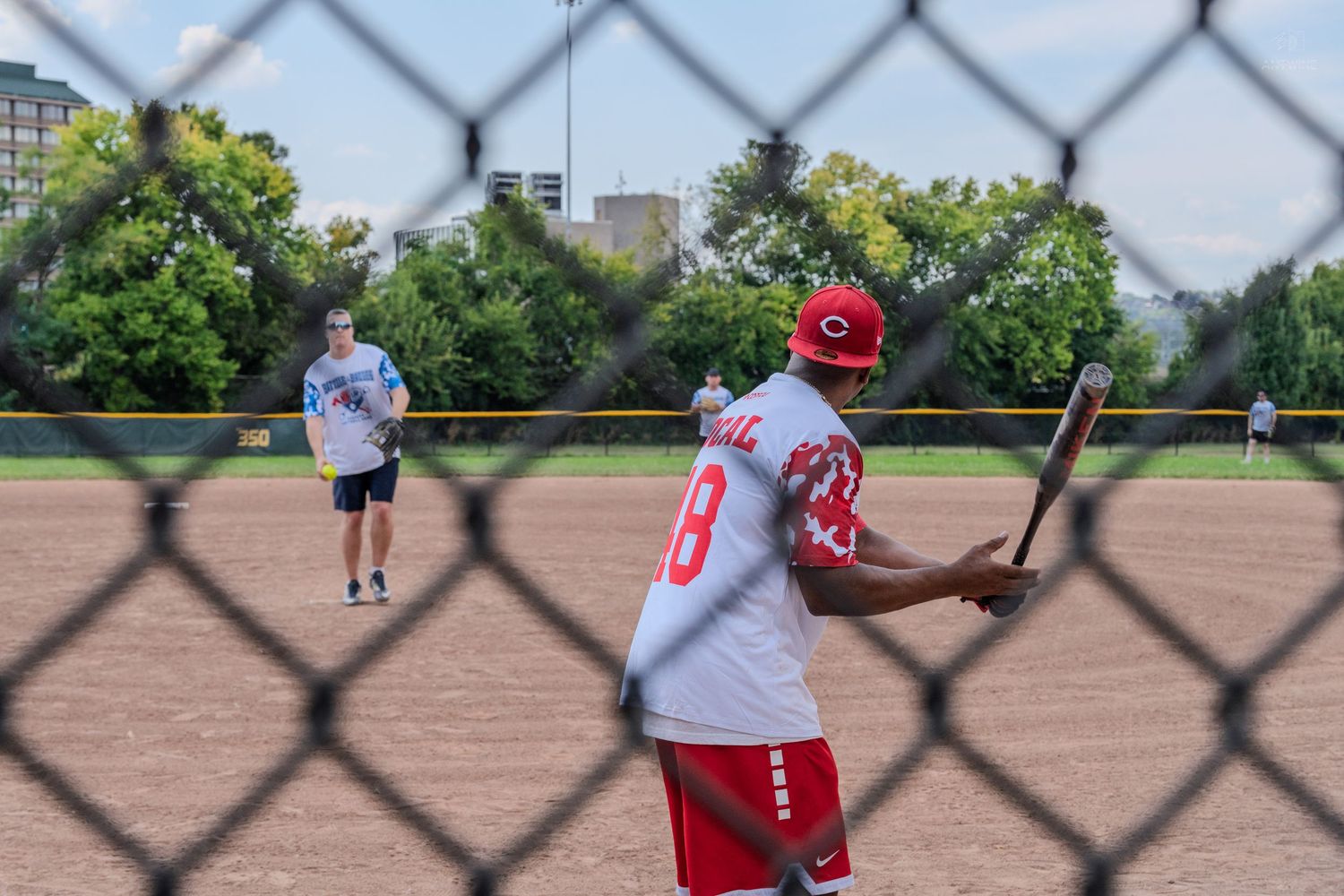 A batter in a red Cincinnati Reds jersey prepares to swing during a softball game.