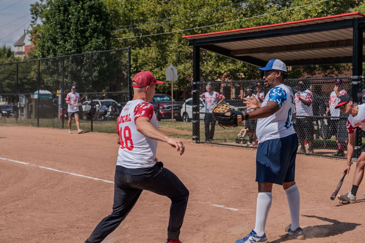 Two softball players on a dirt field during a sunny outdoor game, one pitching and one batting.