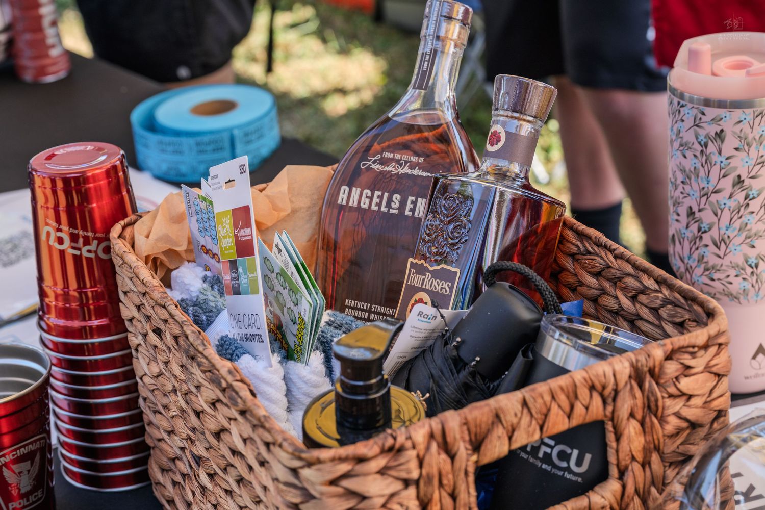 Gift basket with Angel's Envy bourbon bottle and accessories at outdoor event.