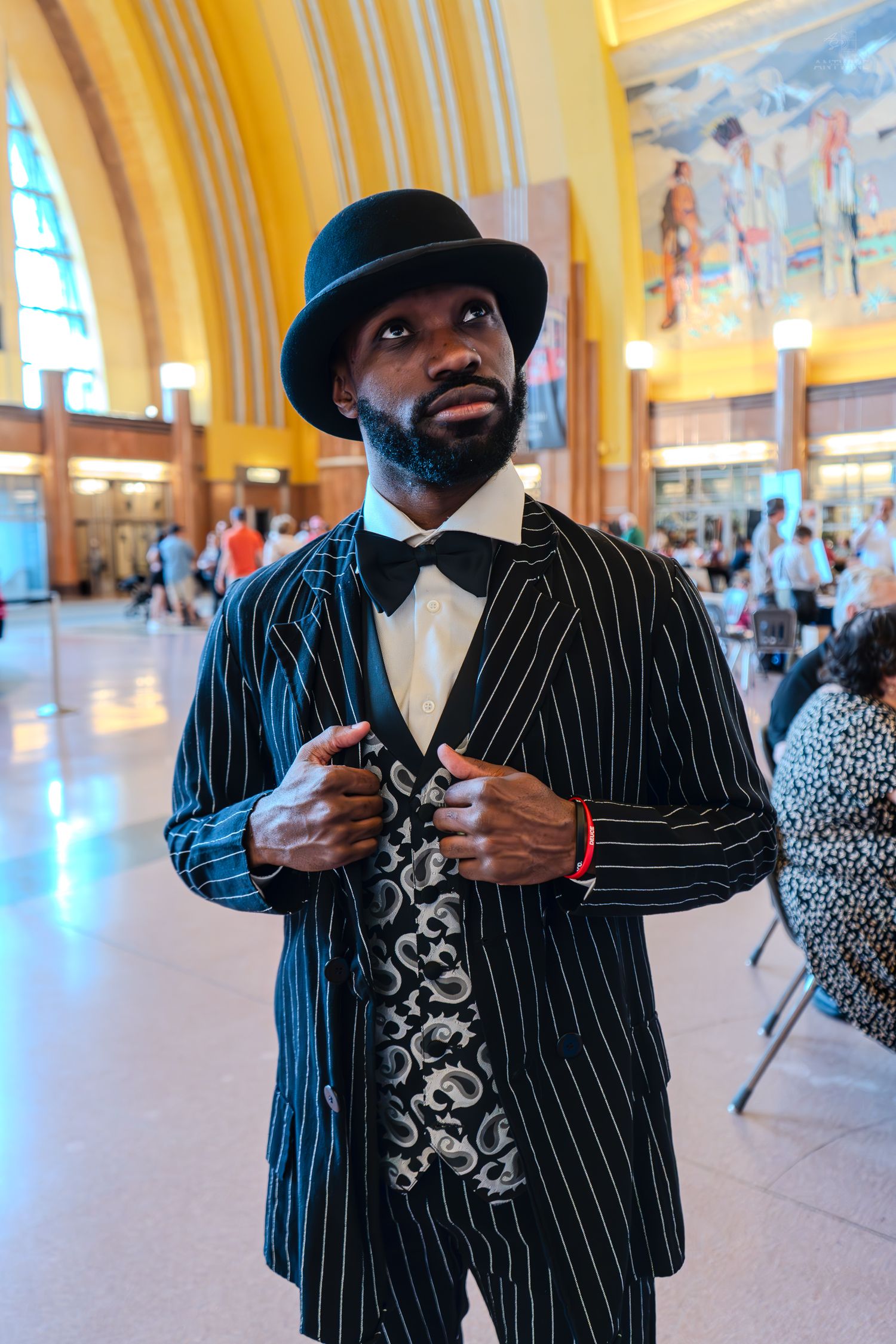 Stylish man in pinstripe suit, bow tie, and bowler hat posing in elegant hall.