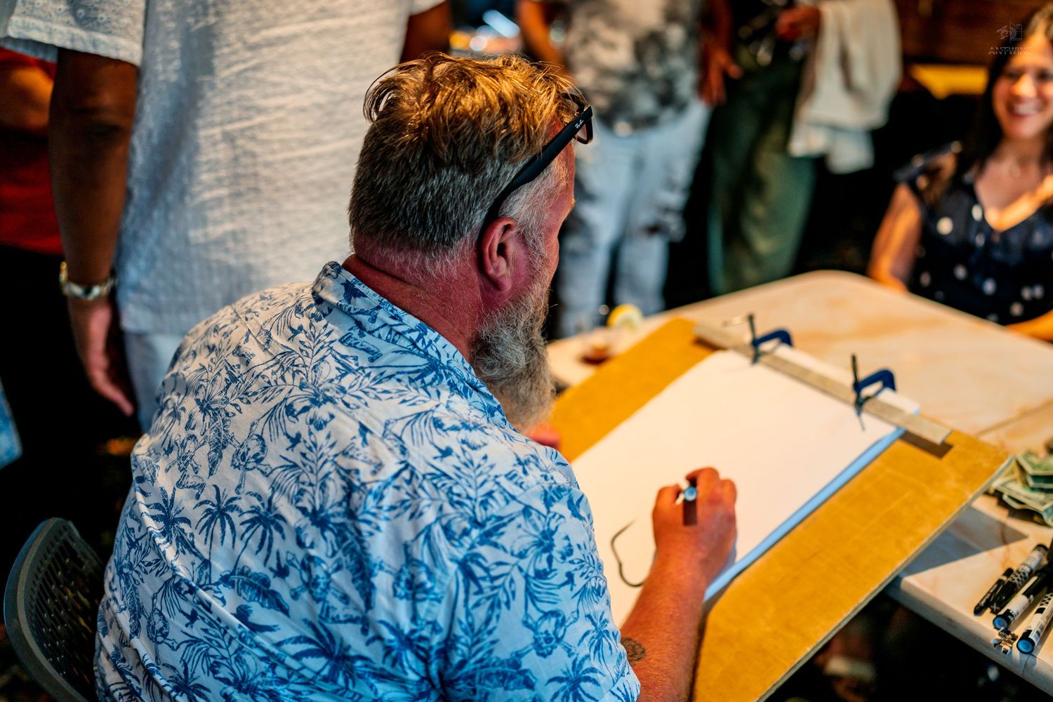 Caricature artist in a floral shirt drawing portraits at a table during a special event.