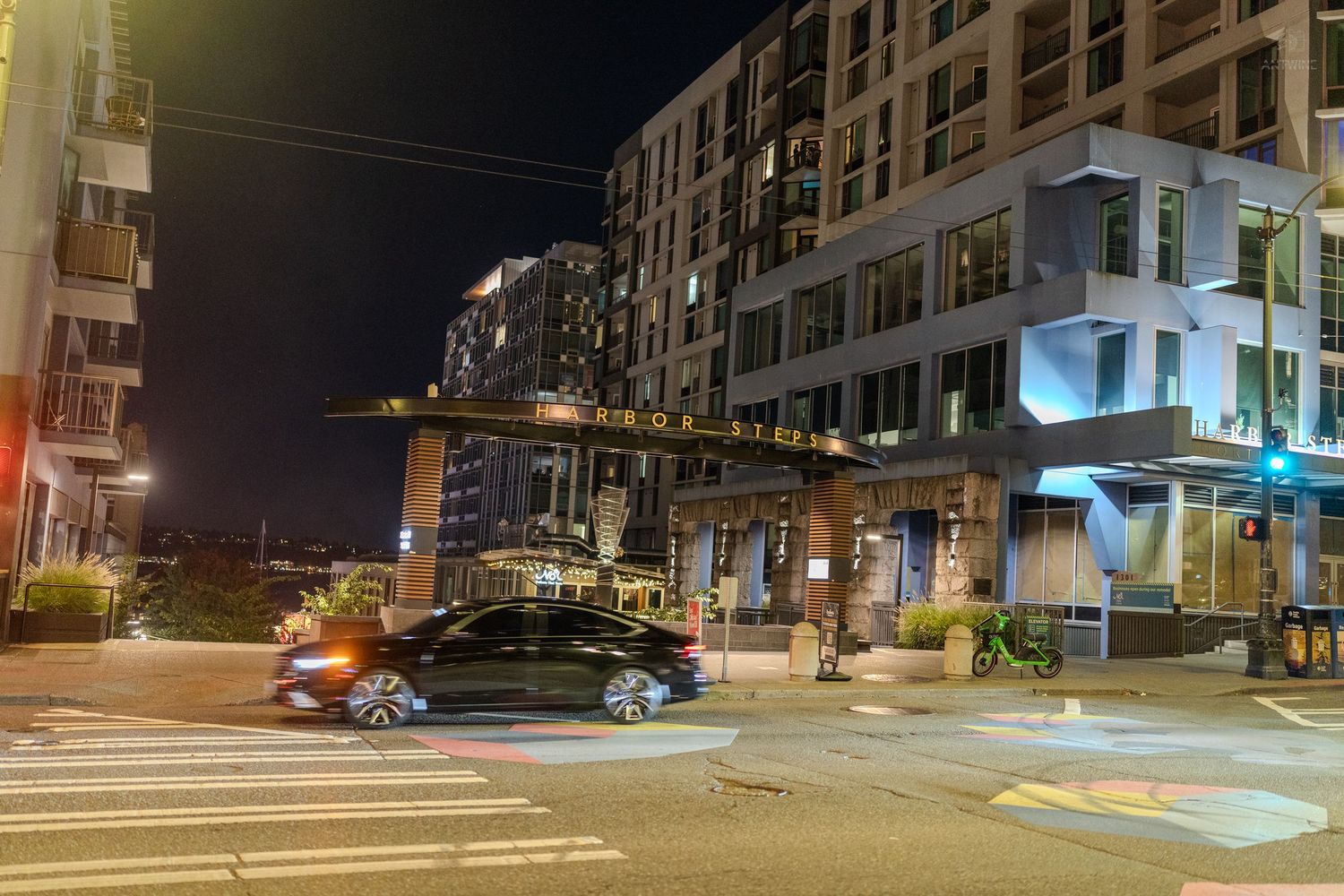 Modern apartment complex illuminated at night with a car passing through an urban intersection.