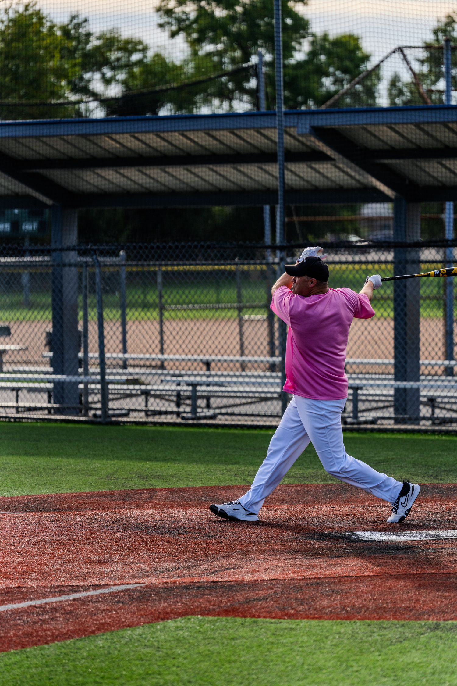 Softball player in pink jersey completes a full follow-through swing during an outdoor recreational game.
