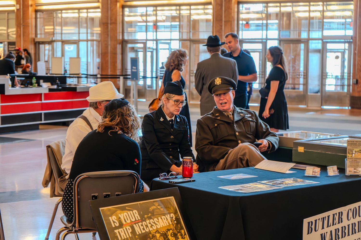 WWII reenactors in military uniforms sit at a display table at a Butler County Warriors history event indoors.