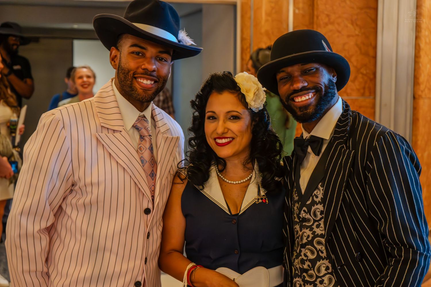 Three people in vintage 1920s costumes smile at a themed party or theatrical event.