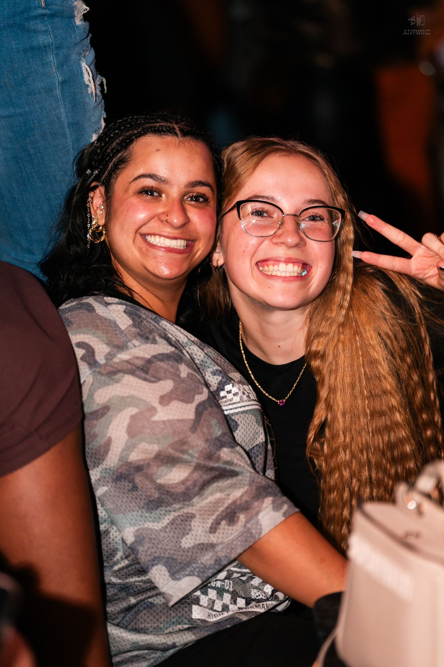 Two smiling women pose together at a nightclub event, one wearing glasses and a black top.