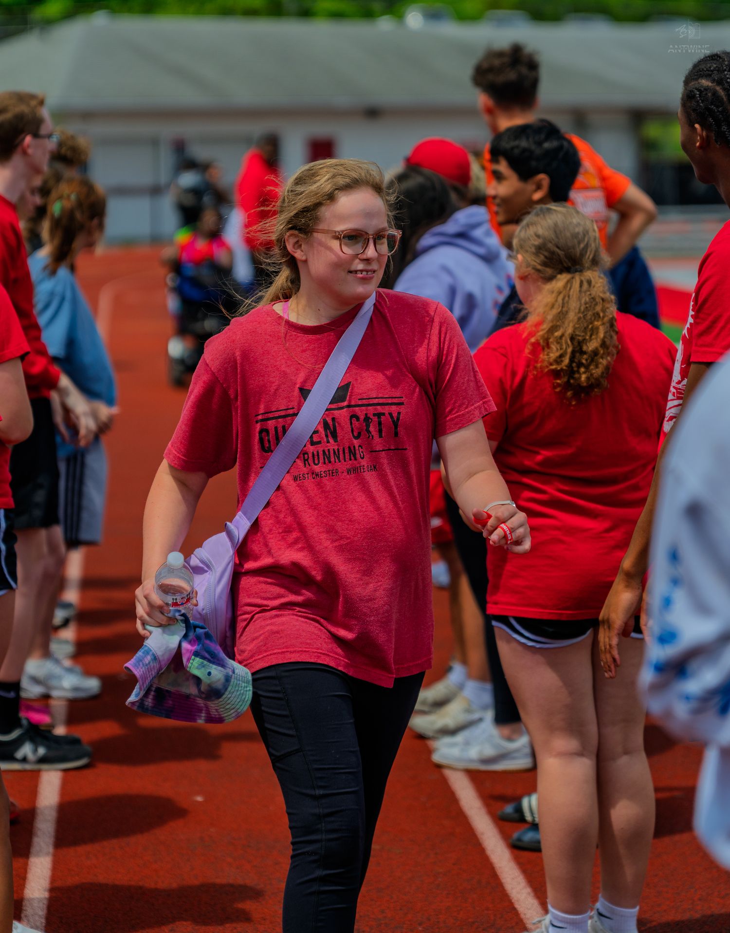 Young girl in red Queen City Running shirt walks on track at outdoor youth athletic event.