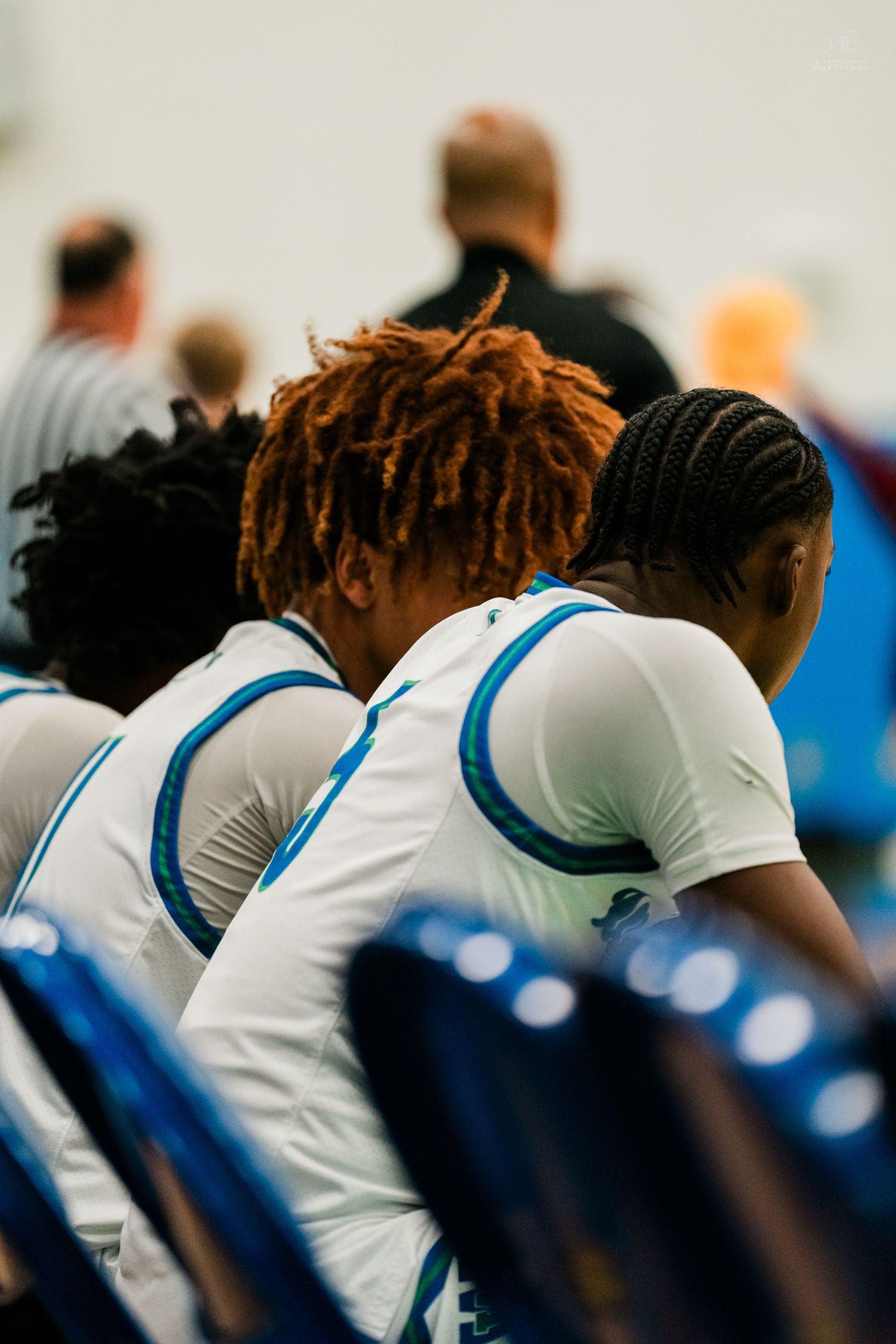 Two basketball players in white and blue uniforms sit on bench during game.