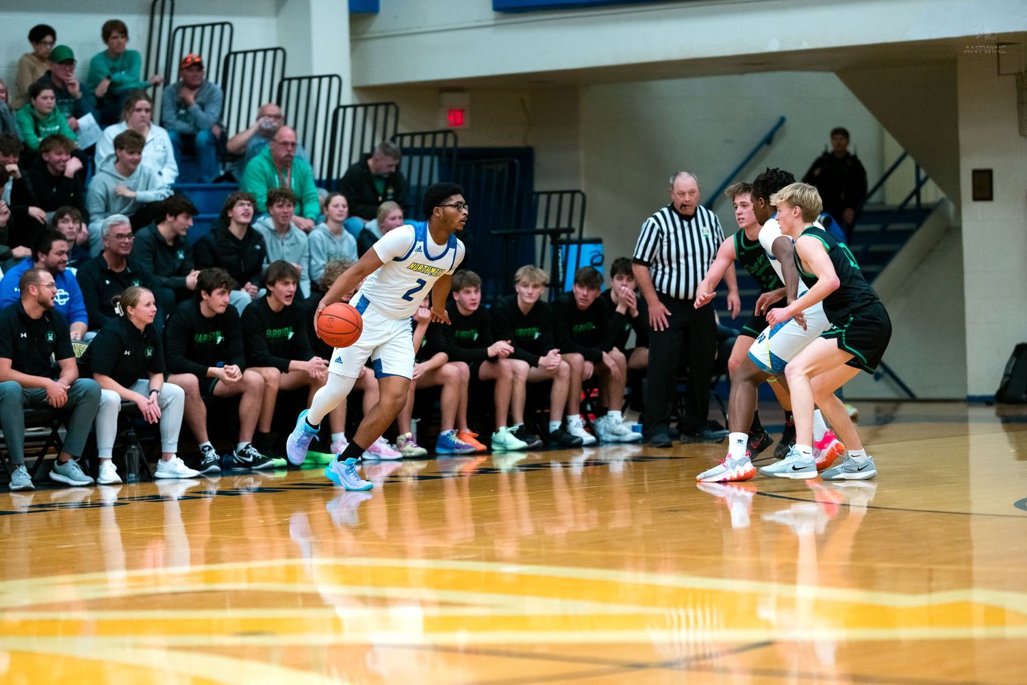 High school basketball player dribbles against a defender during an indoor gymnasium game.