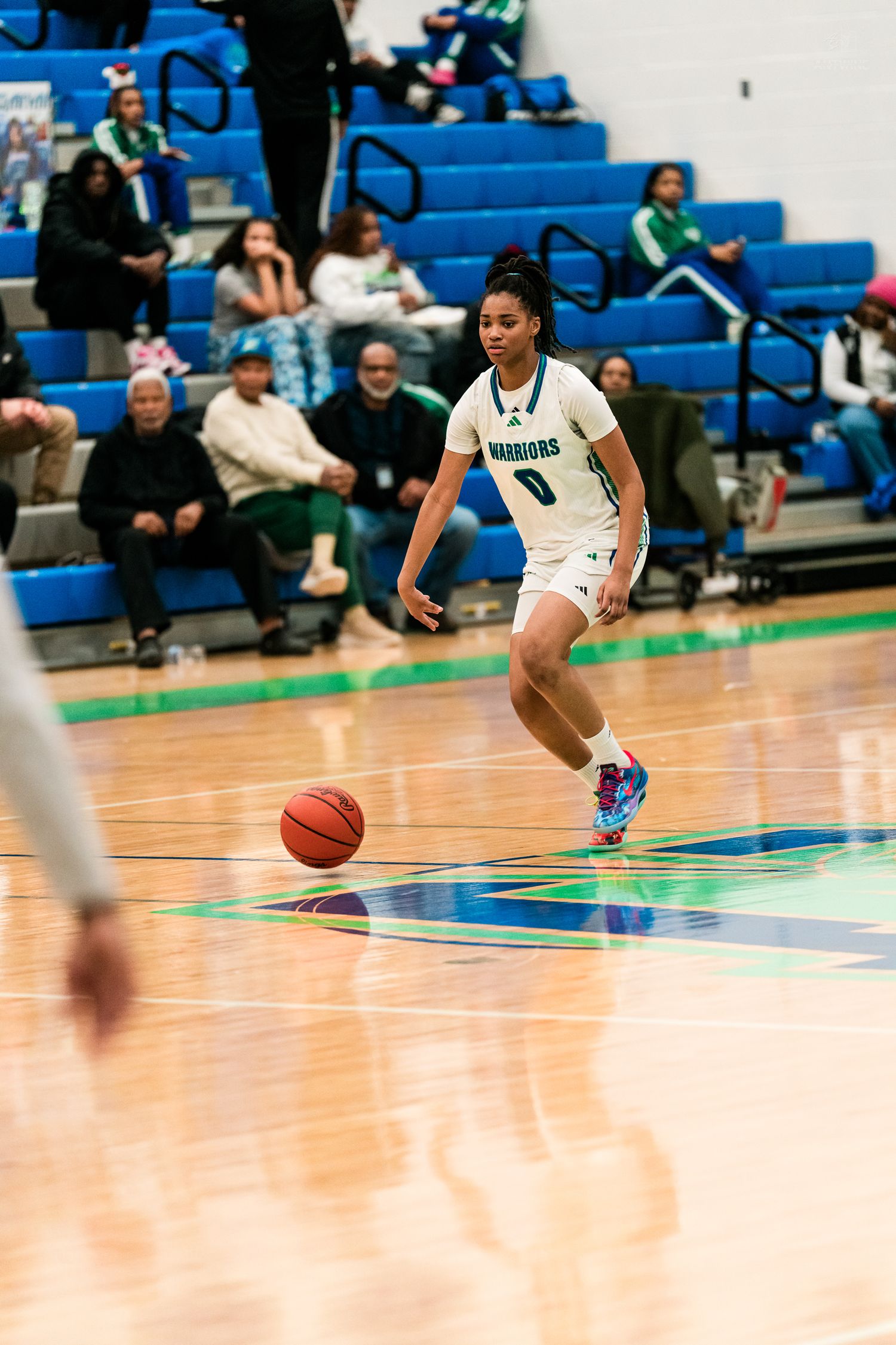 Girls basketball player #0 in teal Warriors uniform dribbles ball during high school basketball game.