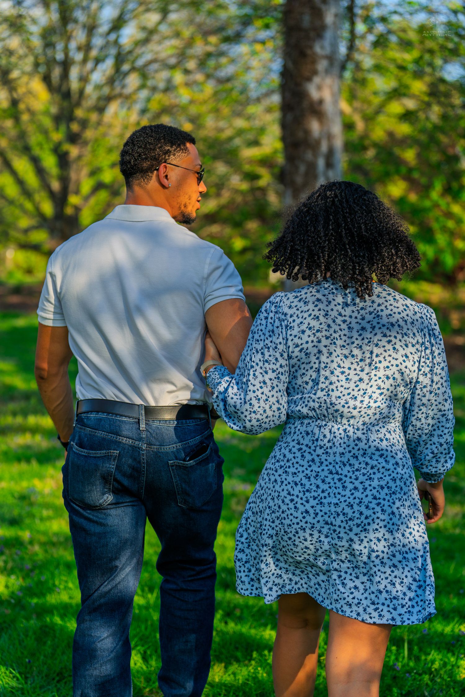 Couple walking hand in hand through a lush green park on a sunny day.
