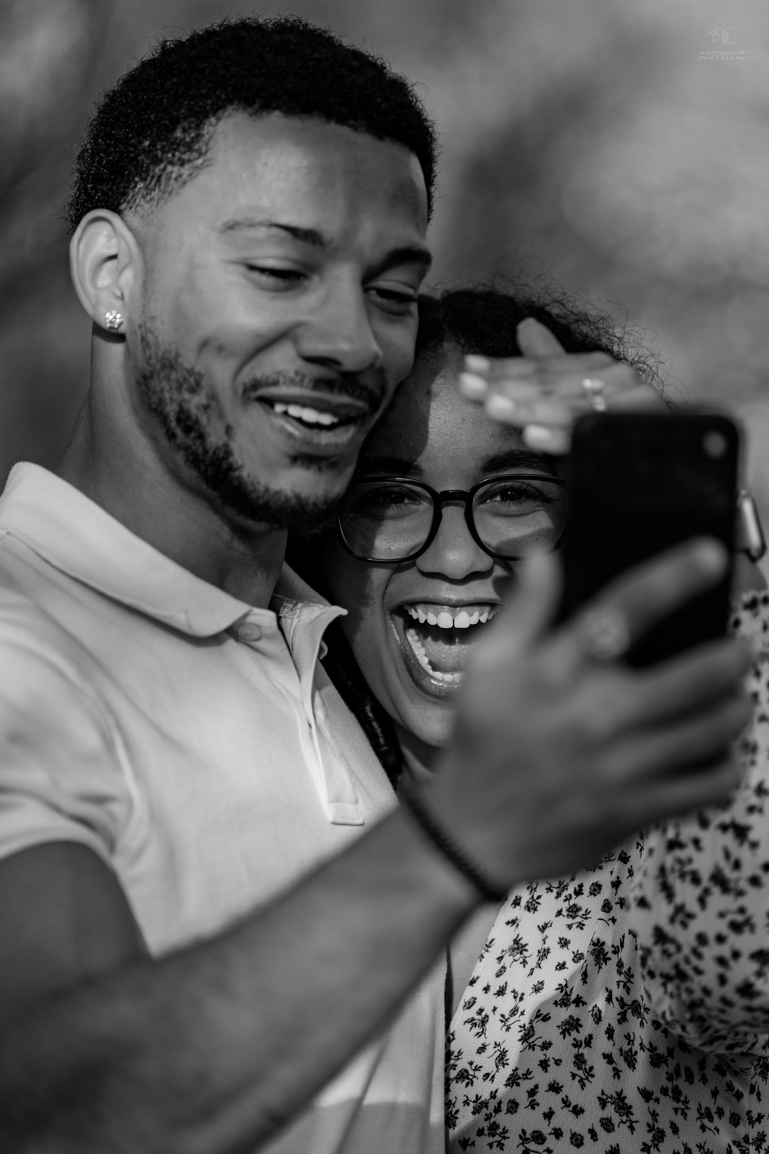 Black and white image of couple sharing a joyful selfie moment outdoors, both laughing and smiling together.