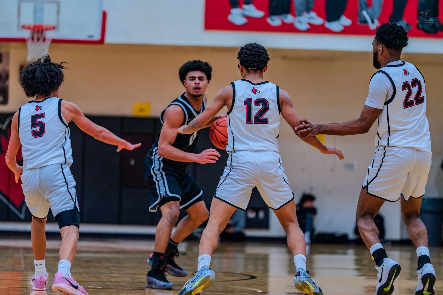 High school basketball player drives through defenders #12 and #22 during an intense indoor basketball game.