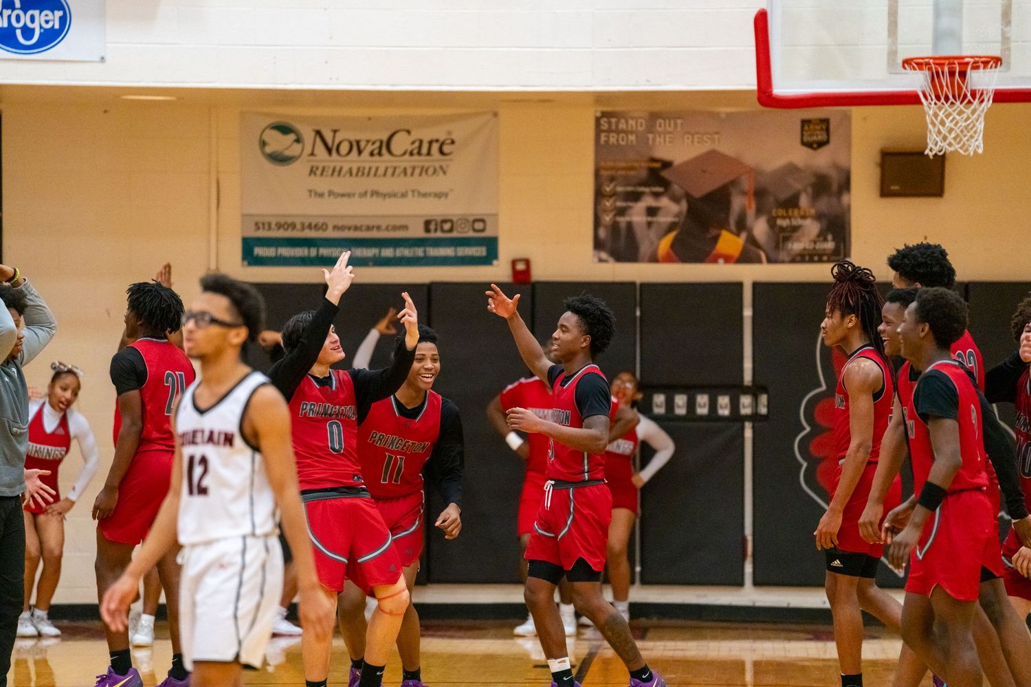 High school basketball players in red uniforms celebrate a successful play during a competitive game.