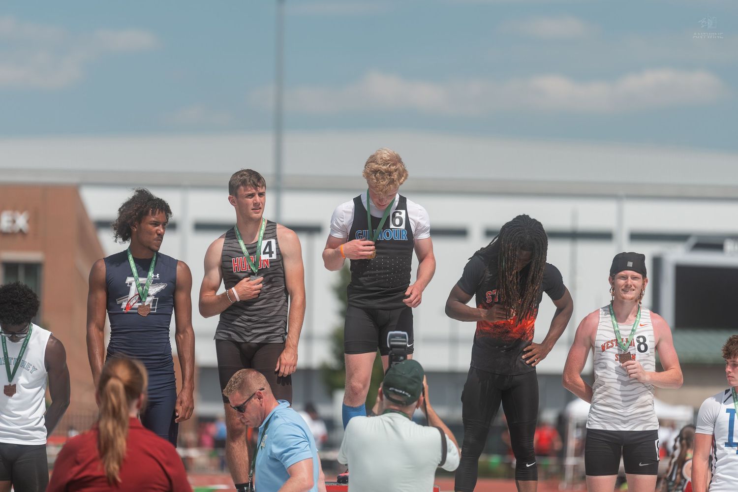 Young male track athletes smile on award podium at sunny OHSAA track and field championship meet.