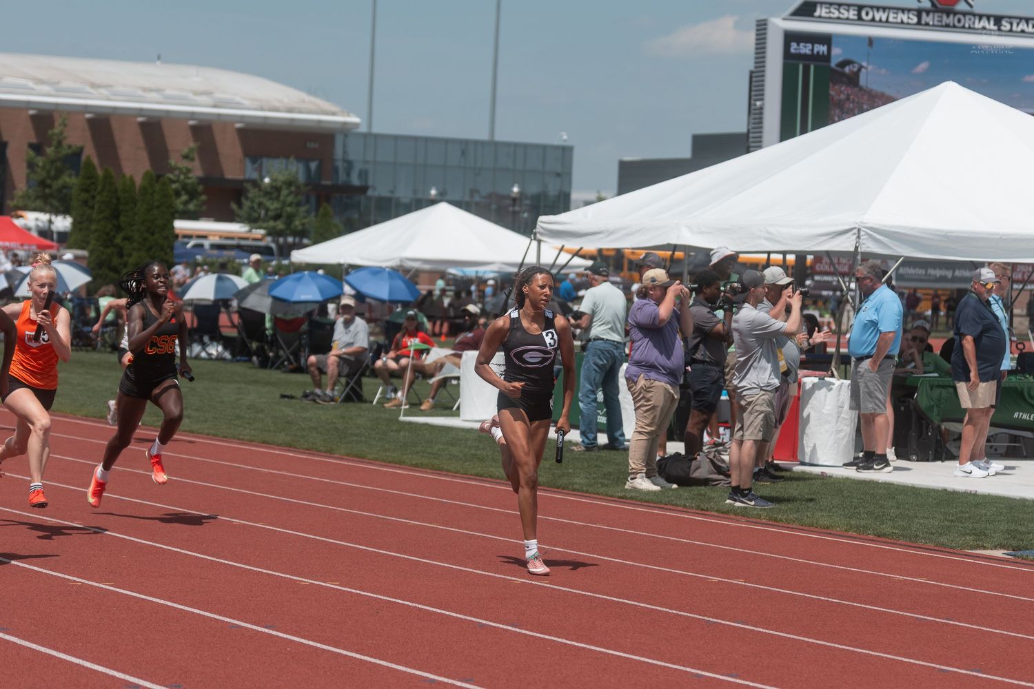 Athletes compete in a sprint race at an OHSAA track and field meet on a red track with spectators watching.