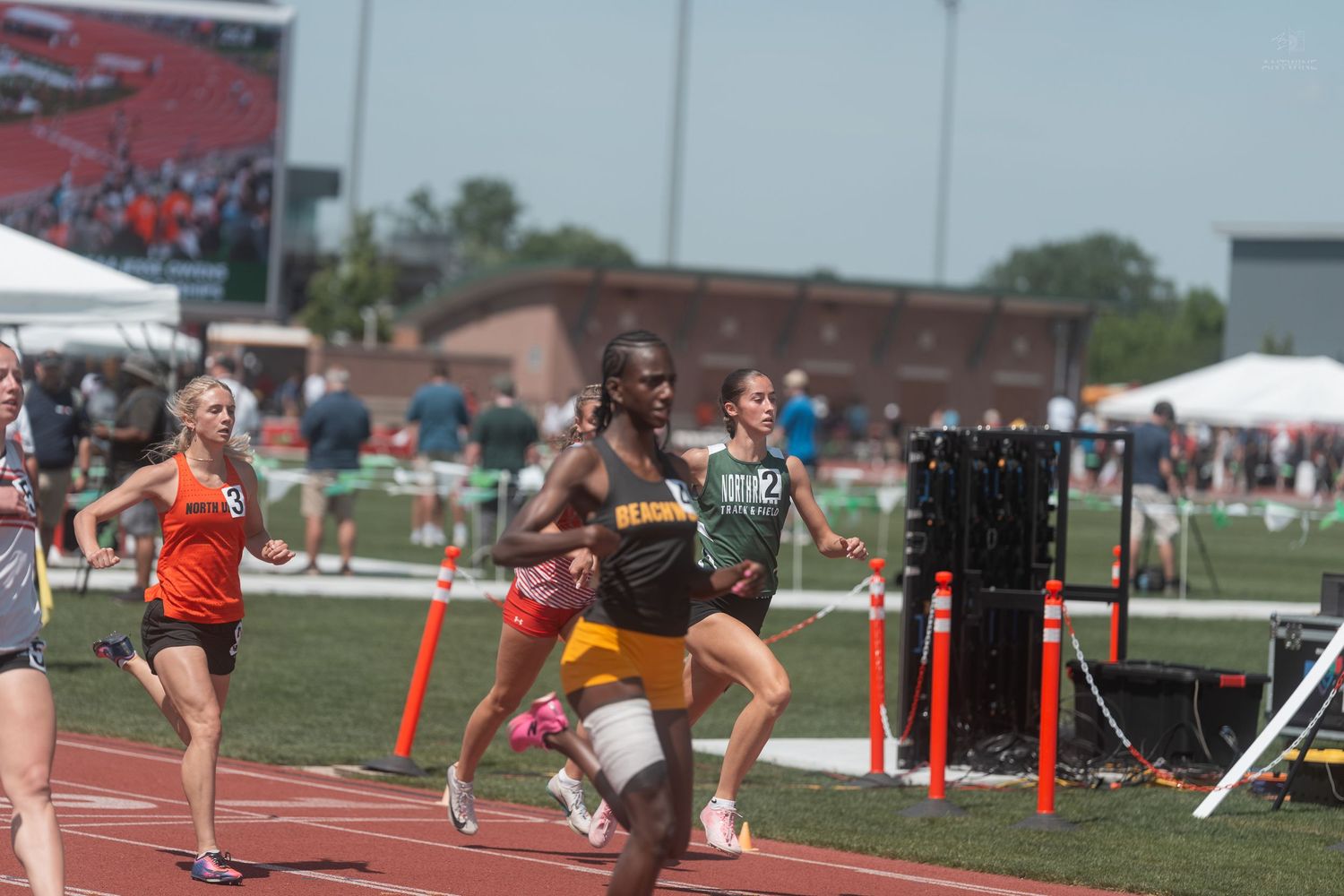 Male track runner leads a relay race on a red track at a high school track and field meet.